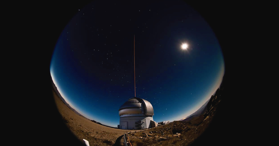 La imagen corresponde a la cúpula y telescopio de Gemini Sur. Se observa un rayo láser en dirección al cielo.